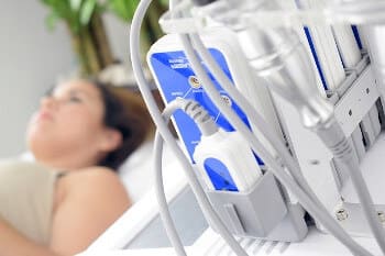 Im Vordergrund ein Ultraschall Gerät und im Hintergrund liegt eine Frau bei der Untersuchung