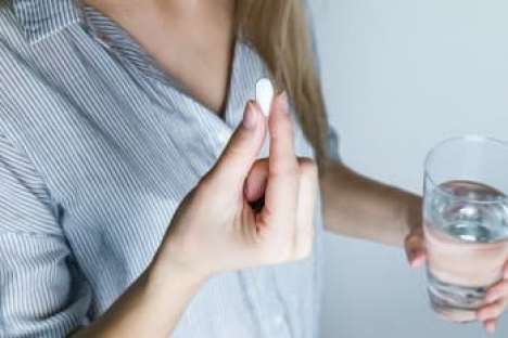 Eine Frau nimmt eine Tablette und hält ein Glas Wasser