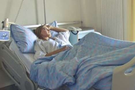 Eine Frau liegt in einem Krankenbett und sieht nachdenklich aus dem Fenster